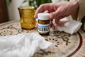 Person taking their allergy medication from a wooden table