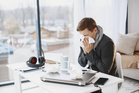 a man at his desk with a tissue over his mouth and nose