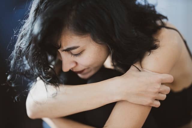 Woman in a black shirt wrapping her arms around herself
