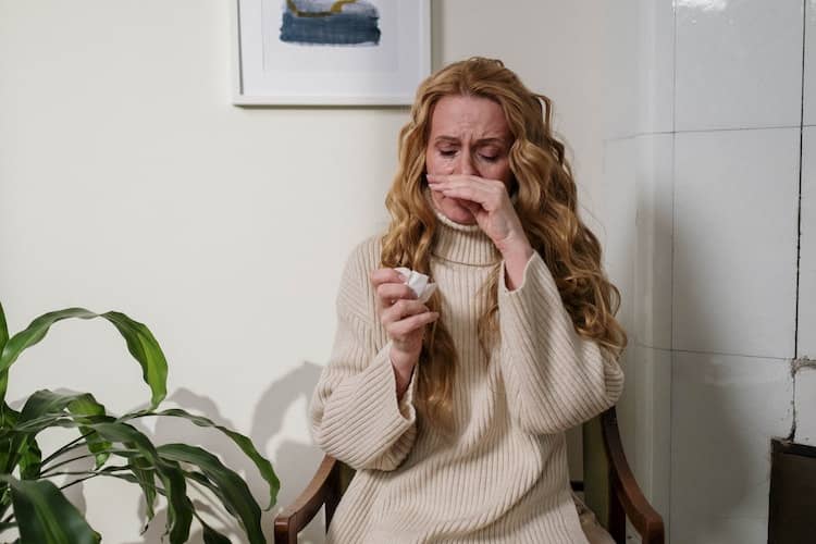 Woman with watery eyes, sneezing and holding a tissue